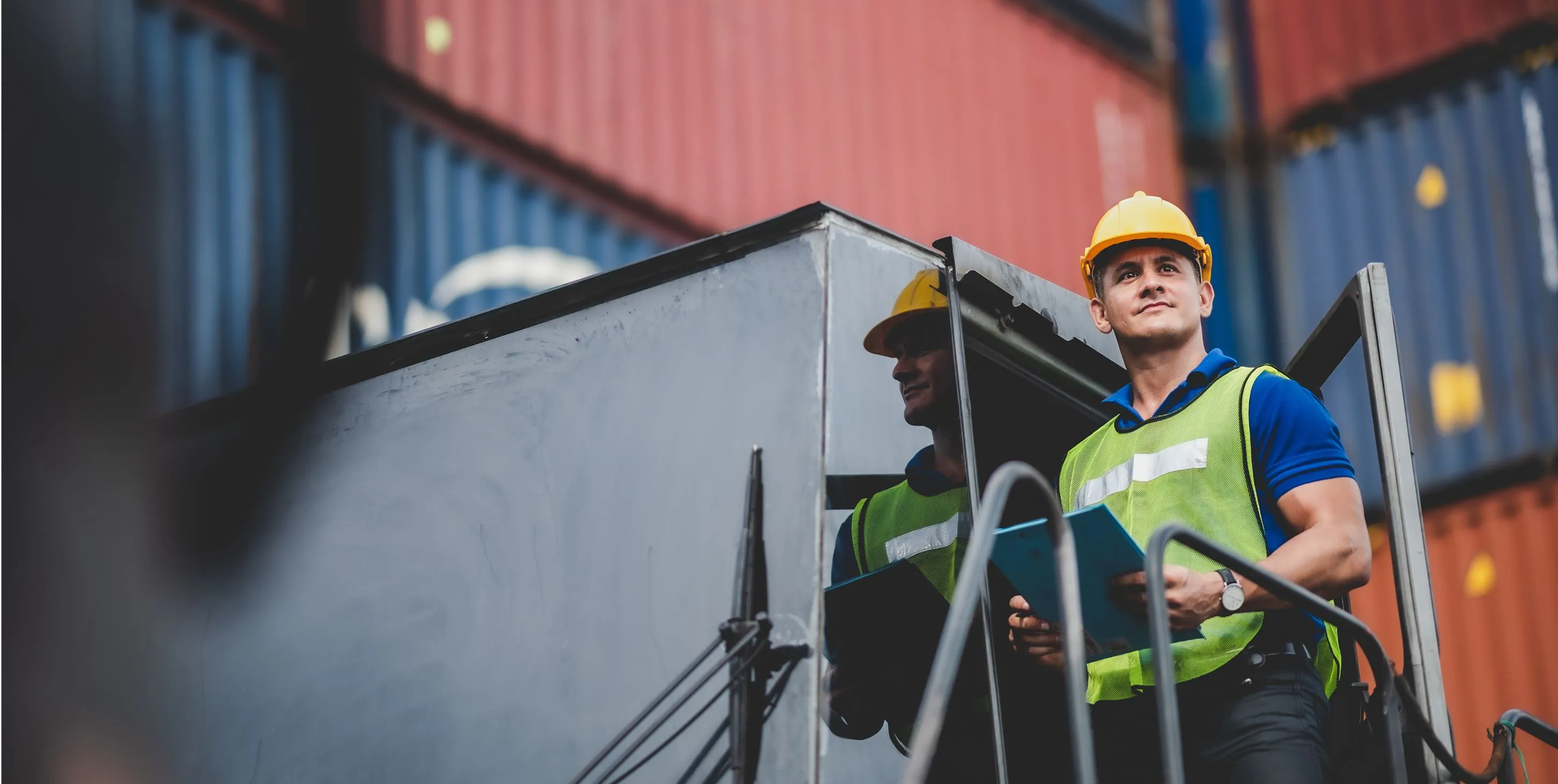 Worker in safety gear with clipboard near shipping containers