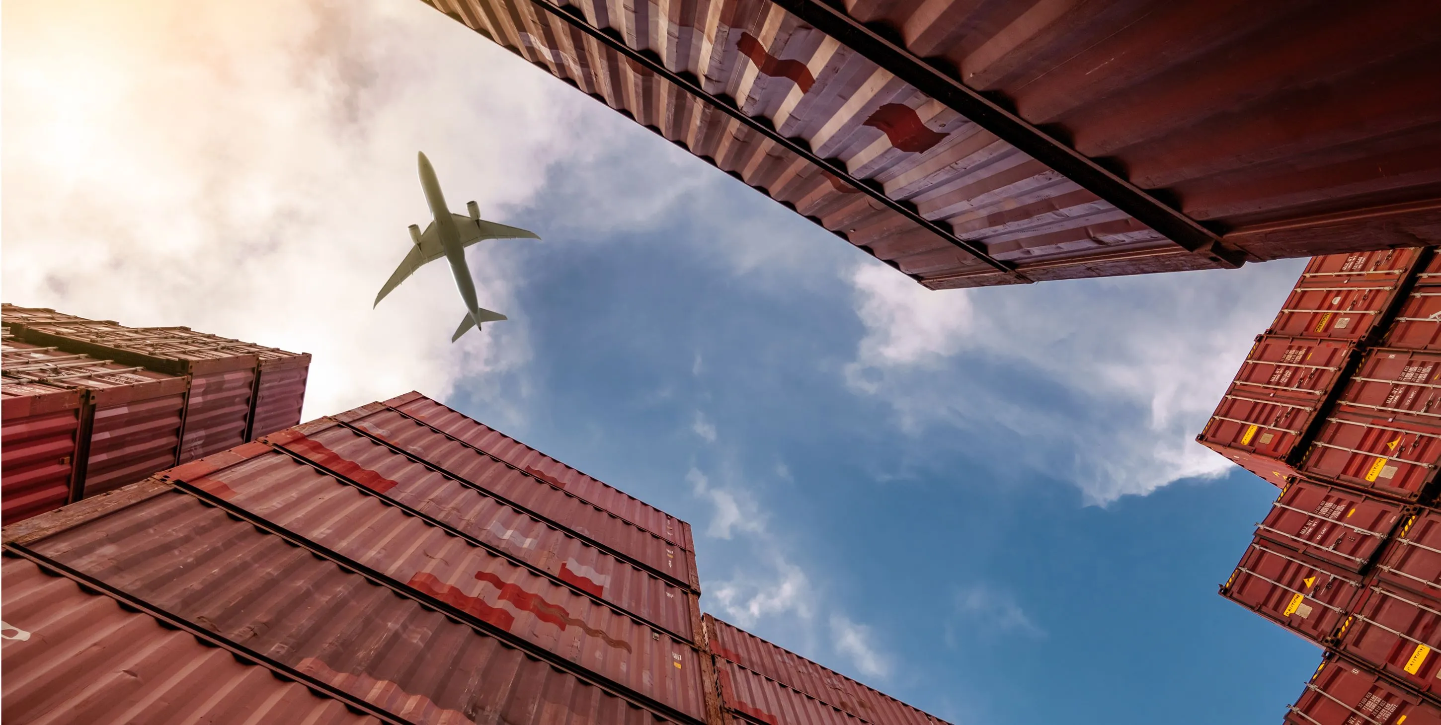 A bottom view of an airplane flying over red containers.