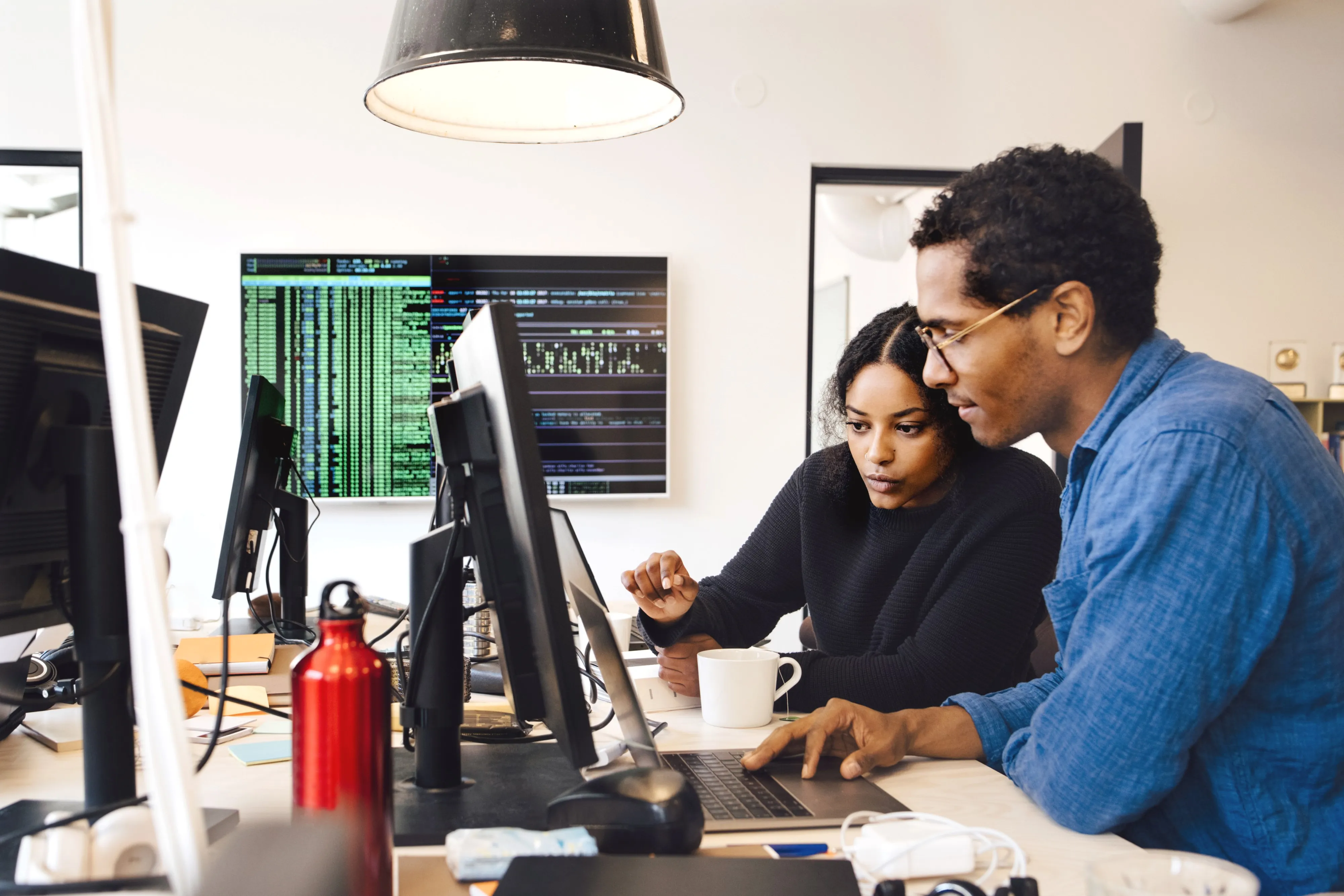 Focused male and female engineers coding over laptop on desk in office